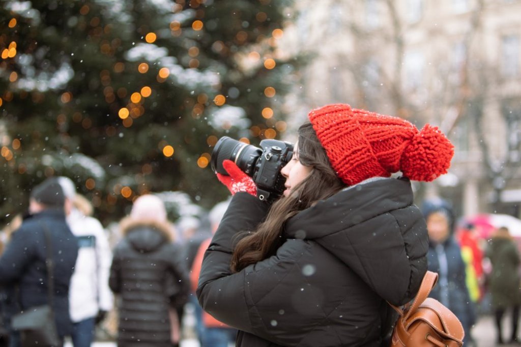 a girl in a red hat taking a picture near a Christmas tree